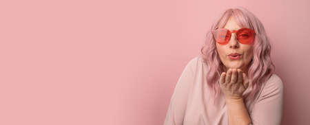 Portrait of happy and positive caucasian woman in orange knitted hat gives an air kiss posing over pink color backgroundの写真素材