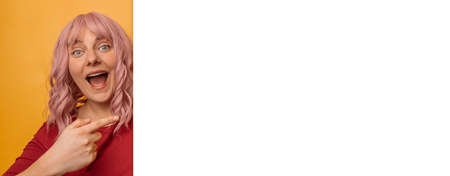 Happy young woman happy positive smile point finger empty space billboard isolated pink backgroundの写真素材