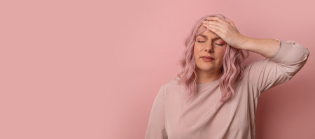 Handsome 30s woman standing with hand on head for pain in head because stress over isolated pink background. Suffering migraine. Hand on head.の写真素材