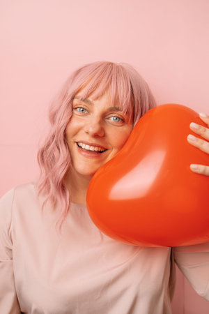 Beautiful happy pretty young smile woman with red heart shape air balloon on a pink background. Valentines Day.の写真素材