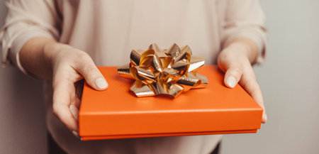Close up shot of woman hands holding surprise gift package box with golden bow on pink pastel background.の写真素材