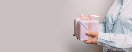 Close up shot of woman hands holding gift package box on pink pastel background with copy space. Congratulations on the holiday. Place for advertising.の写真素材