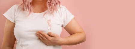 Caucasian woman 30s with a pink satin ribbon on a white t-shirt checks her breasts, breast self-exam (BSE). breast cancer awareness. breast cancer support conceptの写真素材