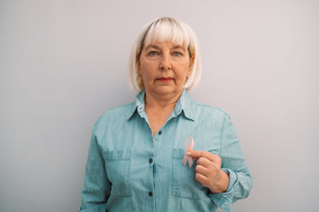Female hand holding pink ribbon in palm symbol of breast cancer awareness on isolated grey background. Healthcare and world cancer dayの写真素材