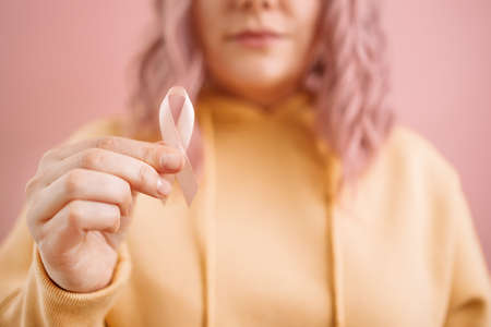 Cropped photo of 30s woman in a yellow sweater with a pink satin ribbon symbolizing International Breast Cancer Day. October rose conceptの写真素材