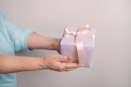 Close up shot of female hands holding violet color gift wrapped with pink ribbon.の写真素材