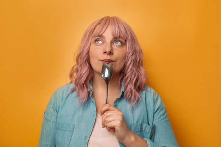 Portrait of hungry woman holding spoon isolated over yellow. Healthy food good taste.の写真素材