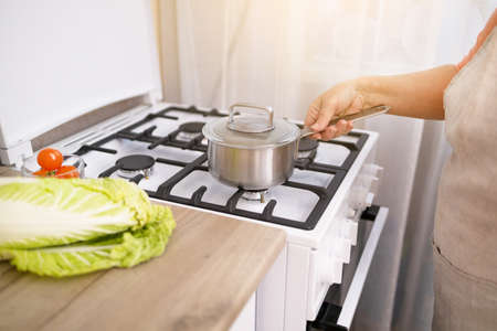 Woman puts stainless steel pot on gas stove in modern kitchen. Cooking utensils conceptの写真素材