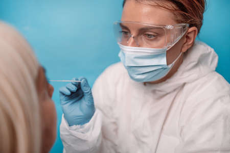 Doctor in protective suit medical mask gloves takes sample from nose of a patient to coronavirus covid-19 antigen test for coronavirusの写真素材