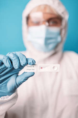 Doctor in blue gloves holding rapid antigen test kit during swab COVID-19 testing over bright blue color background. Pandemic conceptの写真素材