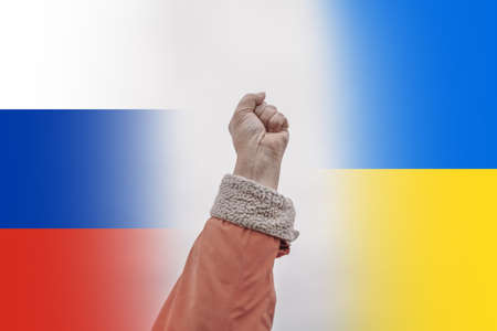Raised fist up against background of Ukrainian and Russian national flags. International political relationship between Ukraine and Russia.の写真素材