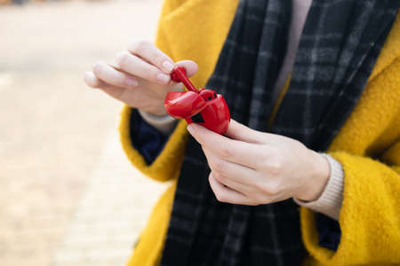 Woman in a beautiful yellow coat. Female hands take out wireless headphones from the case. High quality photoの写真素材