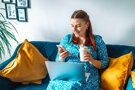 European 30s smile woman drinking coffee and used smartphone on a sofa at home. Red irish setter dog...