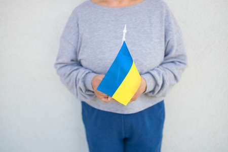 Caucasian hands hold Ukraine nation flag on wall background. People protest against the war in Ukraine.の写真素材