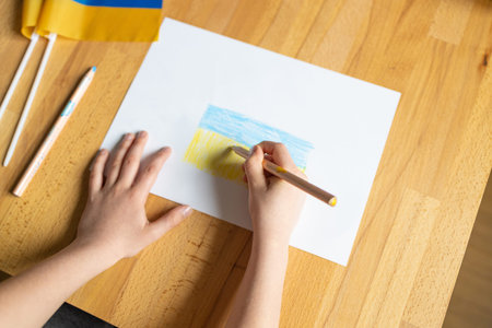 Childs hand draws blue yellow flag of Ukraine on white paper. Peace.