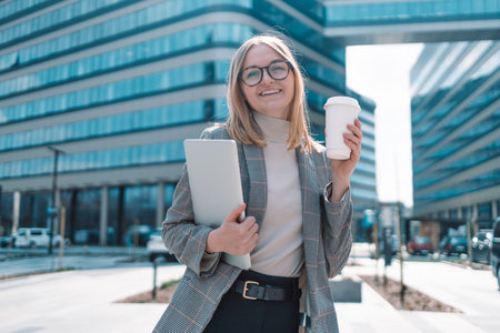 European blonde attractive business woman in trendy clothes with a laptop and take away Bio paper...