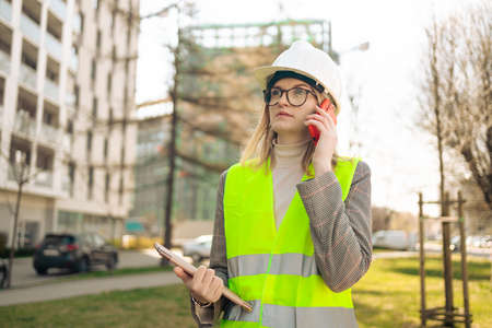 Hard working female construction engineer standing on a construction site. Confident engineer talking on the phone and show casing work in progressの写真素材