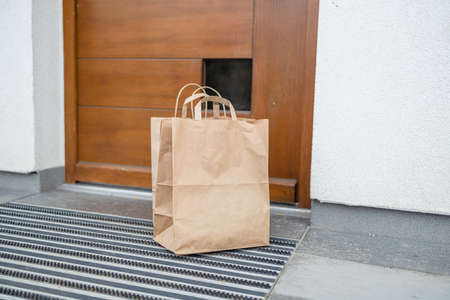 Paper bag with products left by courier of food delivery service during corona virus spreading at front door homeの写真素材