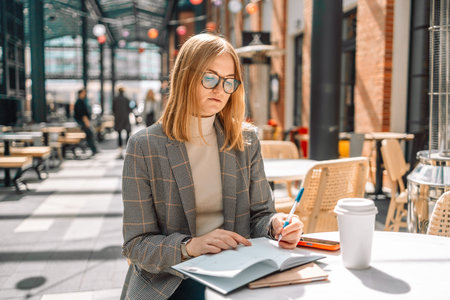 Businesswoman writing on notebook and work with laptop on wooden table, sitting at coffee shop