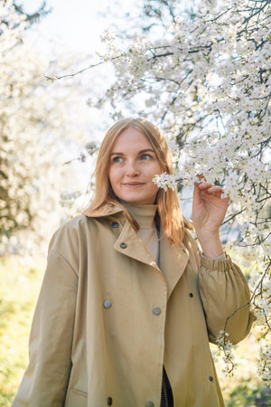 Young woman enjoying scent in blooming spring garden.Travel, freedom and spring vacation. Fashion style.の写真素材