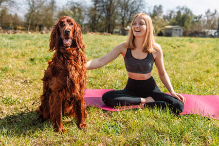 Beautiful blonde woman practice yoga lotus pose with Irish setter dog dog enjoy and relax with yoga...
