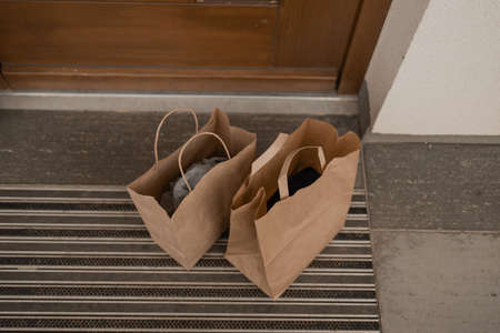 Paper bag with products left by courier of food delivery service during corona virus spreading at front door homeの写真素材
