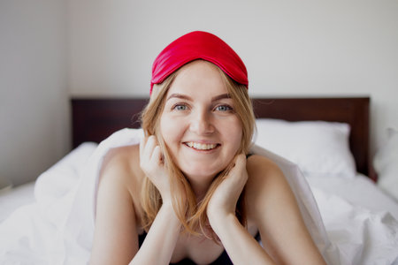 Young beautiful girl smiling after wake up in her bed with white bedclothes early in the morning.の写真素材