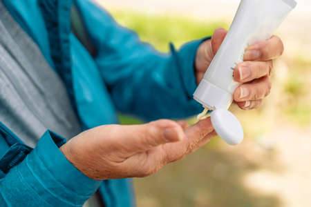 Woman in blue sport clothes applying sunscreen lotion from a white tube while traveling in the mountainsの写真素材