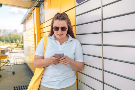 Woman picks up mail from automated self-service post terminal machine. Parcel shipping service or...