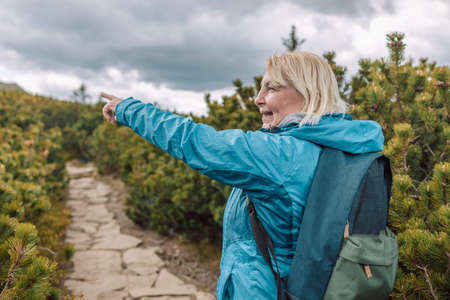 Young Caucasian hiker traveler with backpack adventure gesturing hand finds directions to the mountain nature. Technology internet and travel adventure concept. High quality photoの写真素材