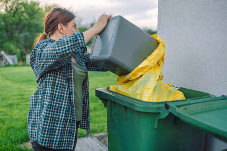 Beautiful young European 30s woman throwing garbage into the trash can in the backyard outdoors near the houseの写真素材