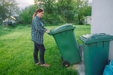 Plastic pollution problem. European 20s girl take out the trash can sorting garbage near a home. Put trash in garbage containers. Volunteers and responsible society.の写真素材