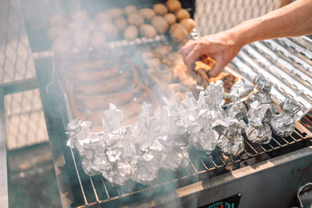 Closeup view of a hot food vendor cooking pork sausages and chops over a hot grill with rising steam, chef uses tongs to flip meat at local agricultural fairの写真素材