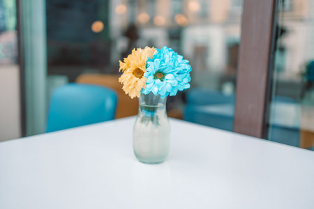 Beautiful blue yellow flowers in glass jar on a wooden table at street cafe for background with blank copy spaceの写真素材