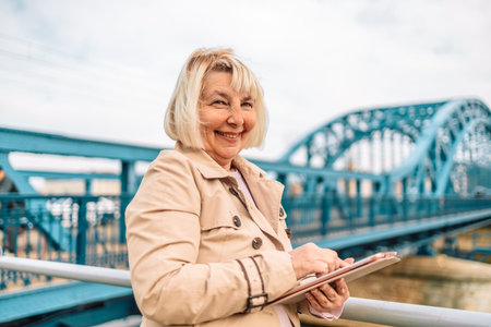 Beautiful 50s business woman in stylish clothes is using a digital tablet and smiling while resting...