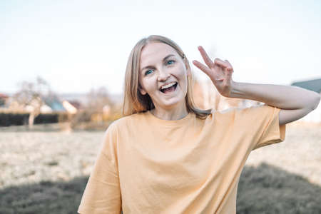 Happy girl with toned skin and white teeth wearing yellow t-shirt making selfie and showing peace signの写真素材