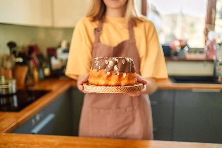 Smiling young blonde woman chef cook in apron standing at the kitchen, showing tasty pie.