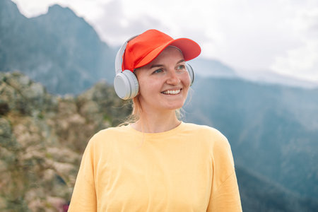 Happy young female traveler with blonde hair in red hat listens to favorite music in wireless...