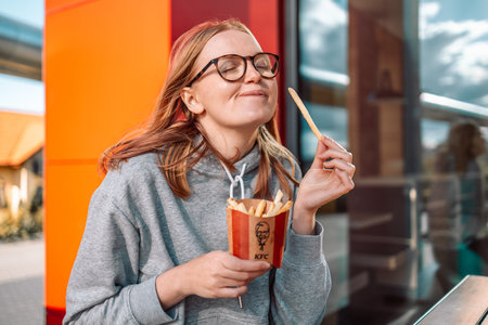 KFC fast food. Krakow, Poland - September 11 2022: Beautiful blonde woman is eating tasting french fries in a KFC restaurant. No diets.のeditorial素材