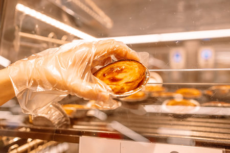 Traditional portuguese dessert. Bakery shop window display. Womans hand in a disposable glove takes...
