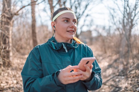 Social media and sport. Young smiling girl making sport and running in the park using her phone to...
