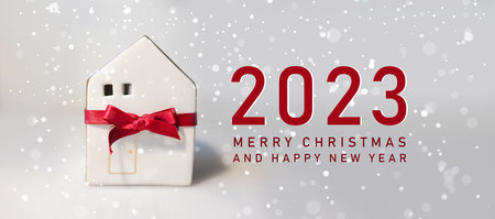 Merry Christmas and 2023 happy new year horizontal banner with small toy model house wrapped in red...