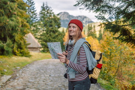 Active young woman holding reading a map while taking a hiking break, having fun and relaxing while...