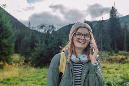 Young female traveler talking on the mountain peak photographs a beautiful mountain landscapeの写真素材