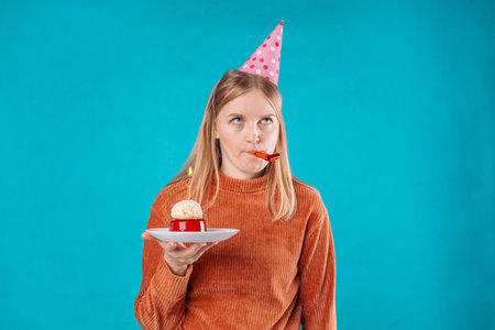Upset 20s woman smeared with cream after eating festive cake expresses negative emotions as feels lonely celebrates Birthday poses against blue backgroundの写真素材