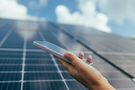 Man using smartphone for controlling photovoltaic solar power station producing green eco friendly...