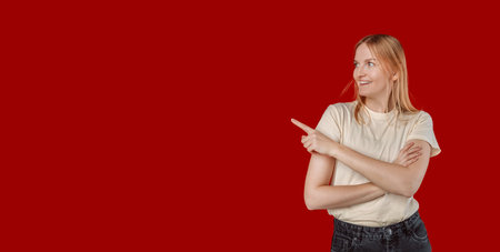 Beautiful young Caucasian woman pointing up to copy space and looking at camera with smile face and happy Pretty girl act like a satisfied product, use for advertising with isolated on red background.の写真素材