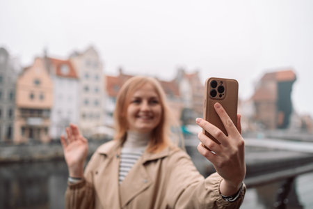 Selfie time. Young happy lady in a spring vacation, walking in the city photographing herself on a...