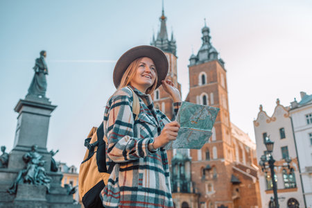 Real view of traveller woman walking on old Market Square in Krakow holding tourist map. Travel and active lifestyle concept. High quality photoの写真素材