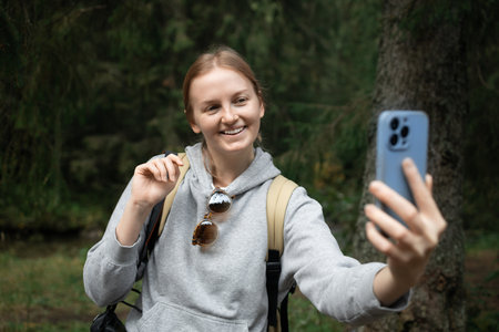 Smiling young woman uses a telephone for take pictures, makes selfies and video calls family from home on mountains background. High quality photoの写真素材
